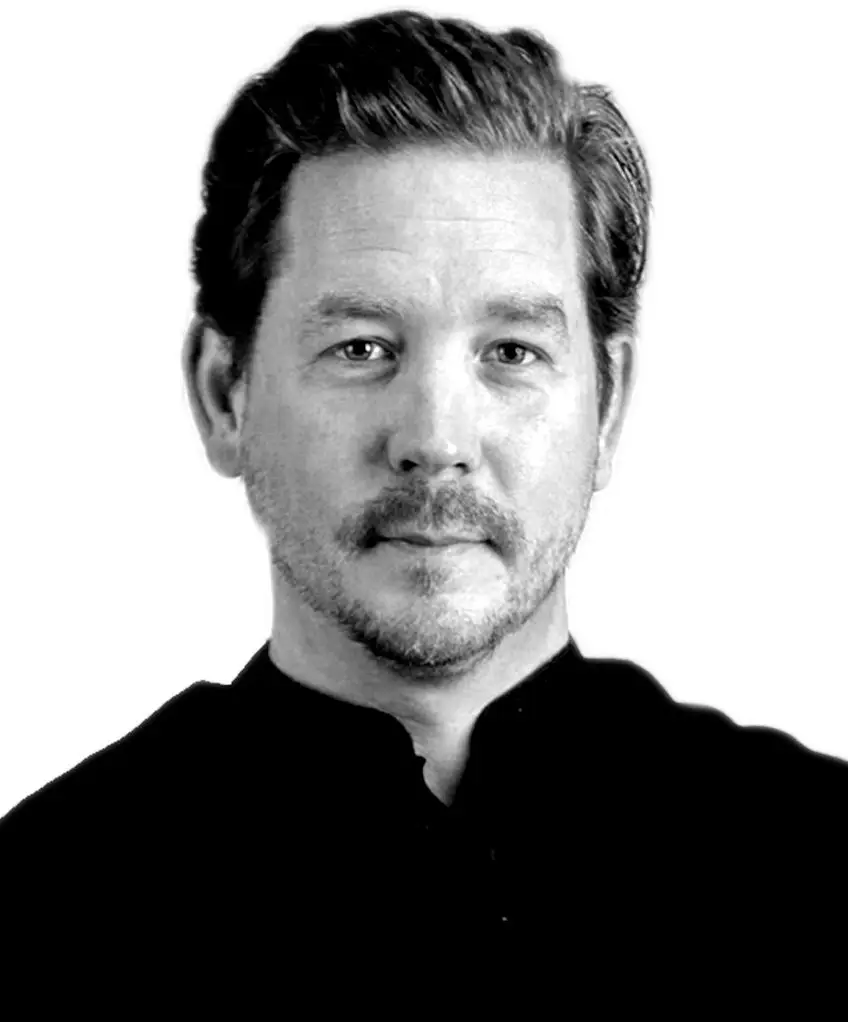 Black and white portrait of a man with short hair and a slight beard wearing a dark shirt.