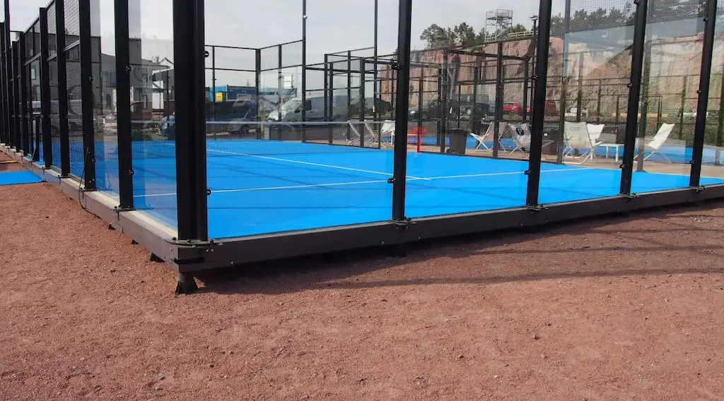 Outdoor padel court featuring a blue playing surface and glass walls for visibility.