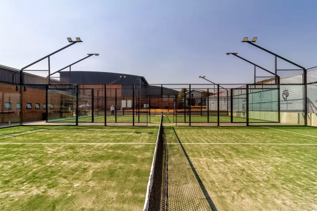 Two padel tennis courts with artificial turf and glass walls under a clear sky.