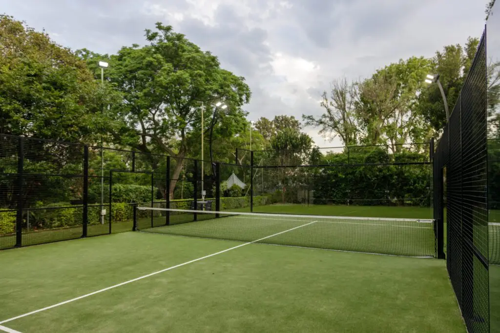 A well-maintained tennis court featuring a green playing surface, surrounded by trees and a black net, ideal for tennis enthusiasts.