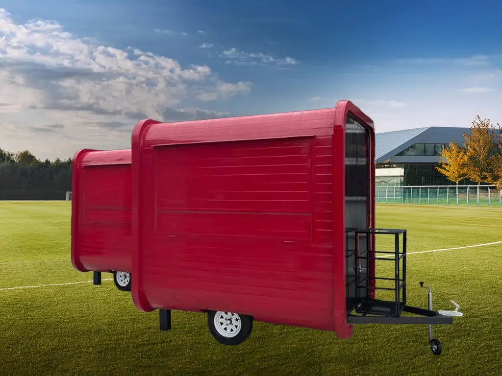 Red mobile food trailer with two compartments and a serving window on a grassy field.