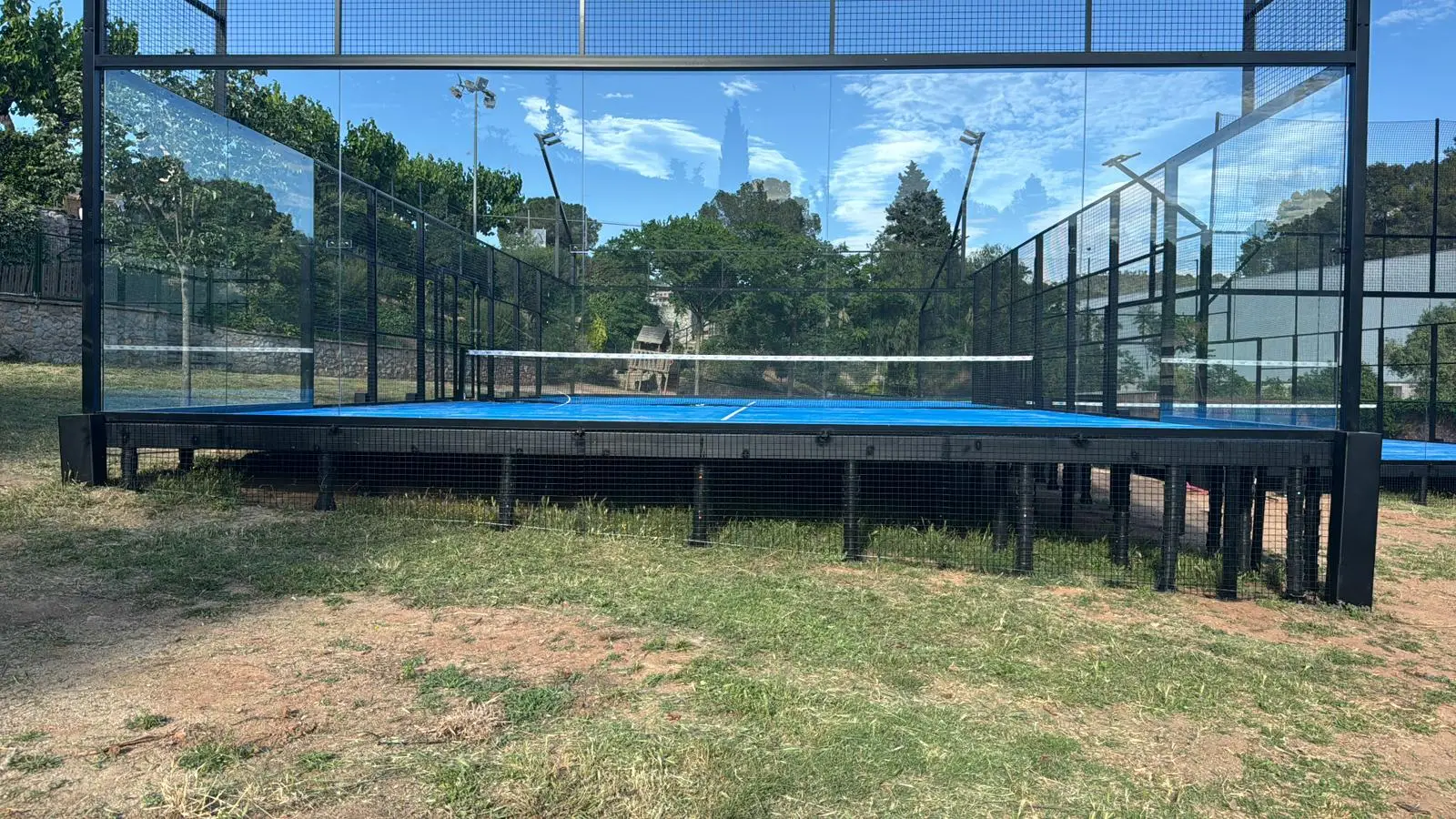 A padel court featuring glass walls and a blue playing surface in an outdoor setting.
