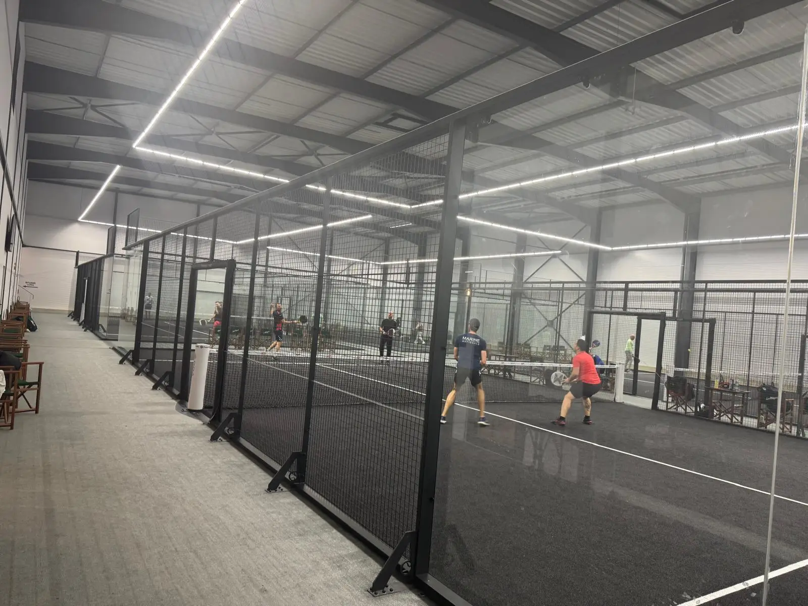 Players engaged in a game of padel tennis on an indoor court with glass walls and netting.