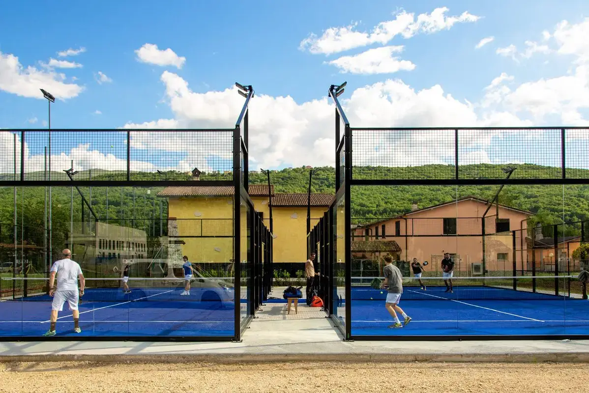 Two padel tennis courts with players engaged in a match under a blue sky